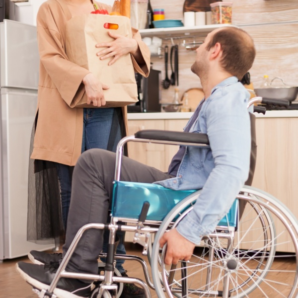 Homme en fauteuil roulant cuisine avec aide.