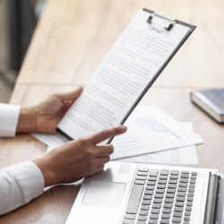 Mains tenant un document écrit, à côté d'un ordinateur portable.