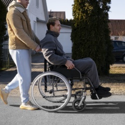 Personne poussant un fauteuil roulant sur le trottoir.